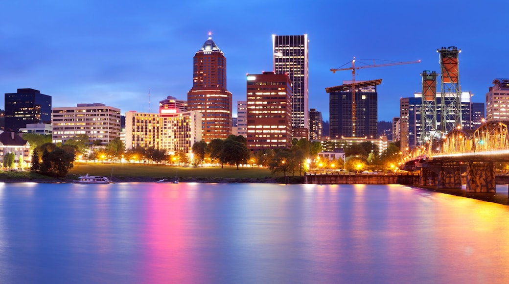 A city skyline with illuminated buildings and a bridge over a calm river.