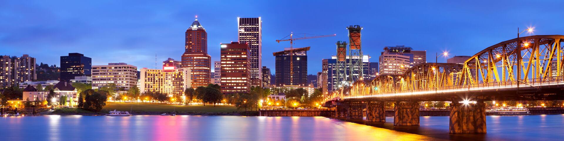 A city skyline with illuminated buildings and a bridge over a calm river.