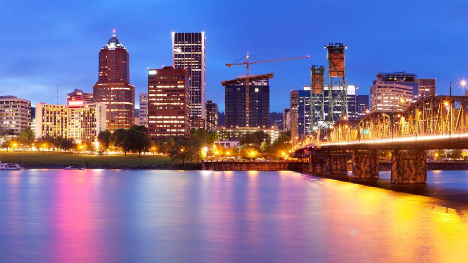 A city skyline with illuminated buildings and a bridge over a calm river.