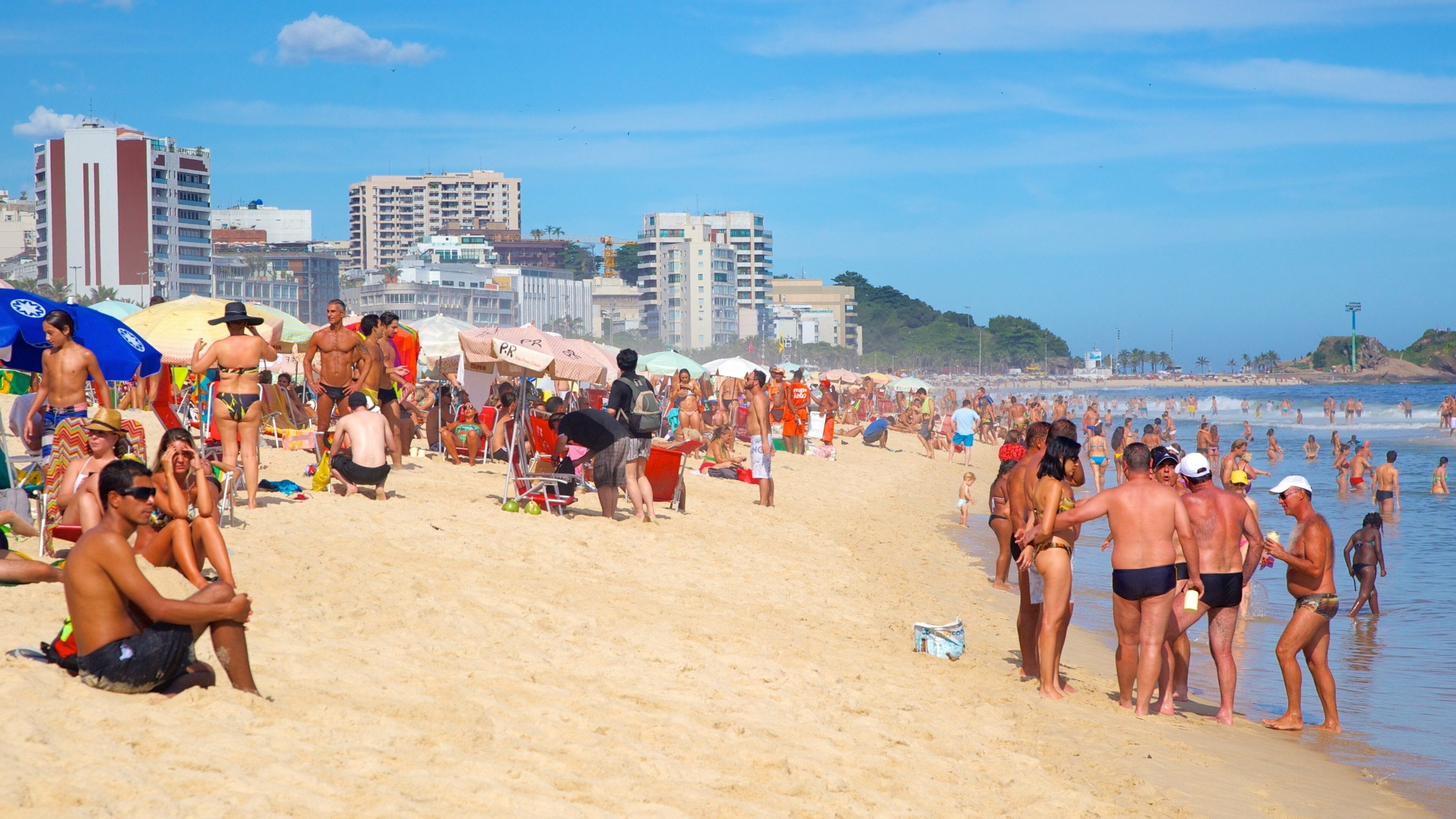 A crowded beach with people sunbathing and swimming.