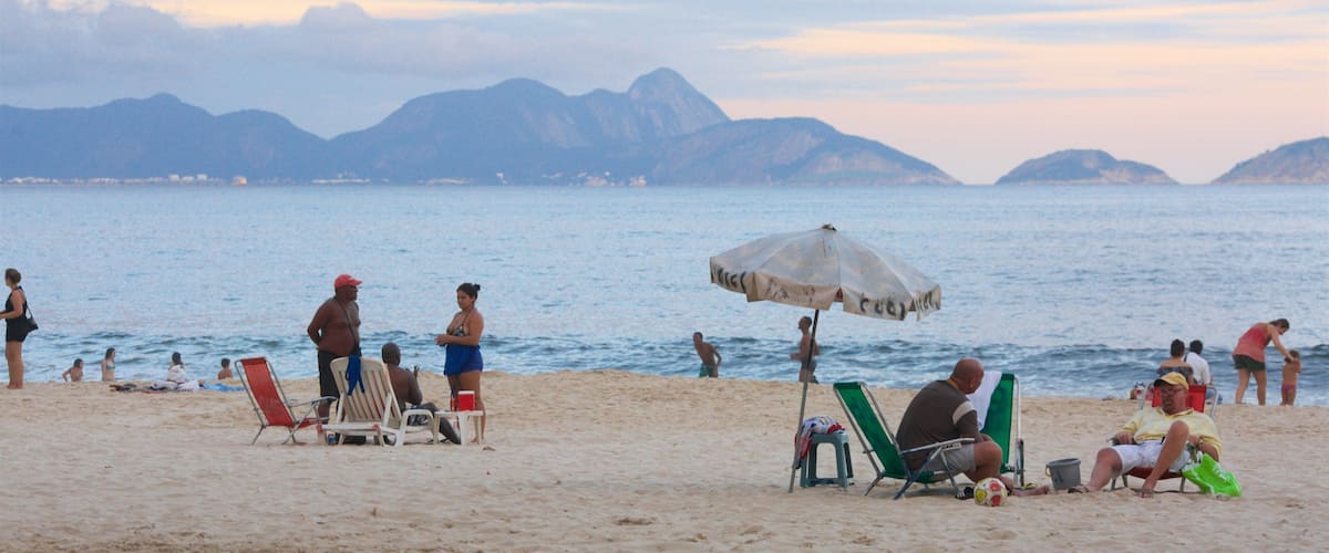 A beach with people relaxing, a soccer ball, and mountains in the background.