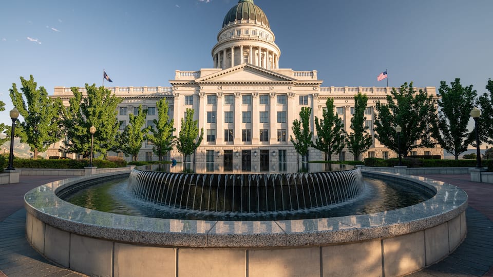 A large government building with a central dome, surrounded by a circular water feature and trees.
