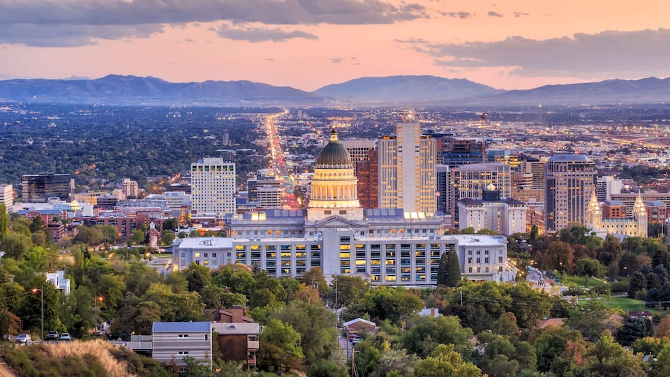 A cityscape with a prominent building with a dome, surrounded by modern high-rise buildings and a mountainous backdrop.