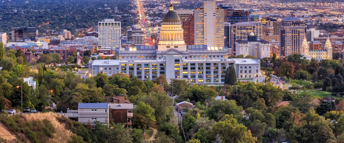 A cityscape with a prominent building with a dome, surrounded by modern high-rise buildings and a mountainous backdrop.