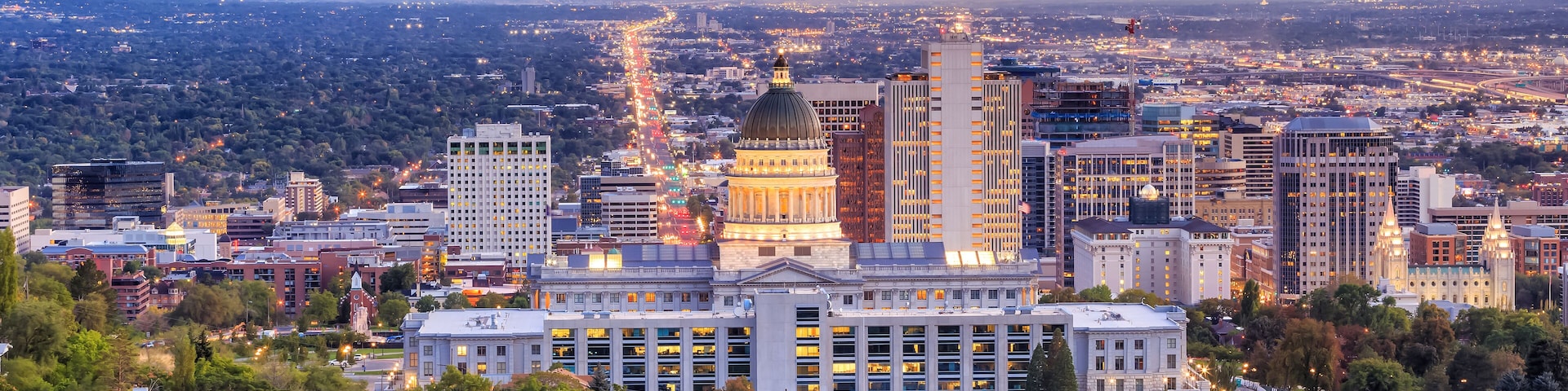 A cityscape with a prominent building with a dome, surrounded by modern high-rise buildings and a mountainous backdrop.