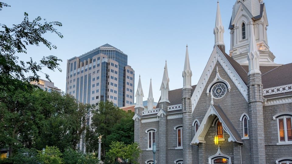 A historic church with pointed spires and a clock tower, surrounded by lush gardens and modern buildings.
