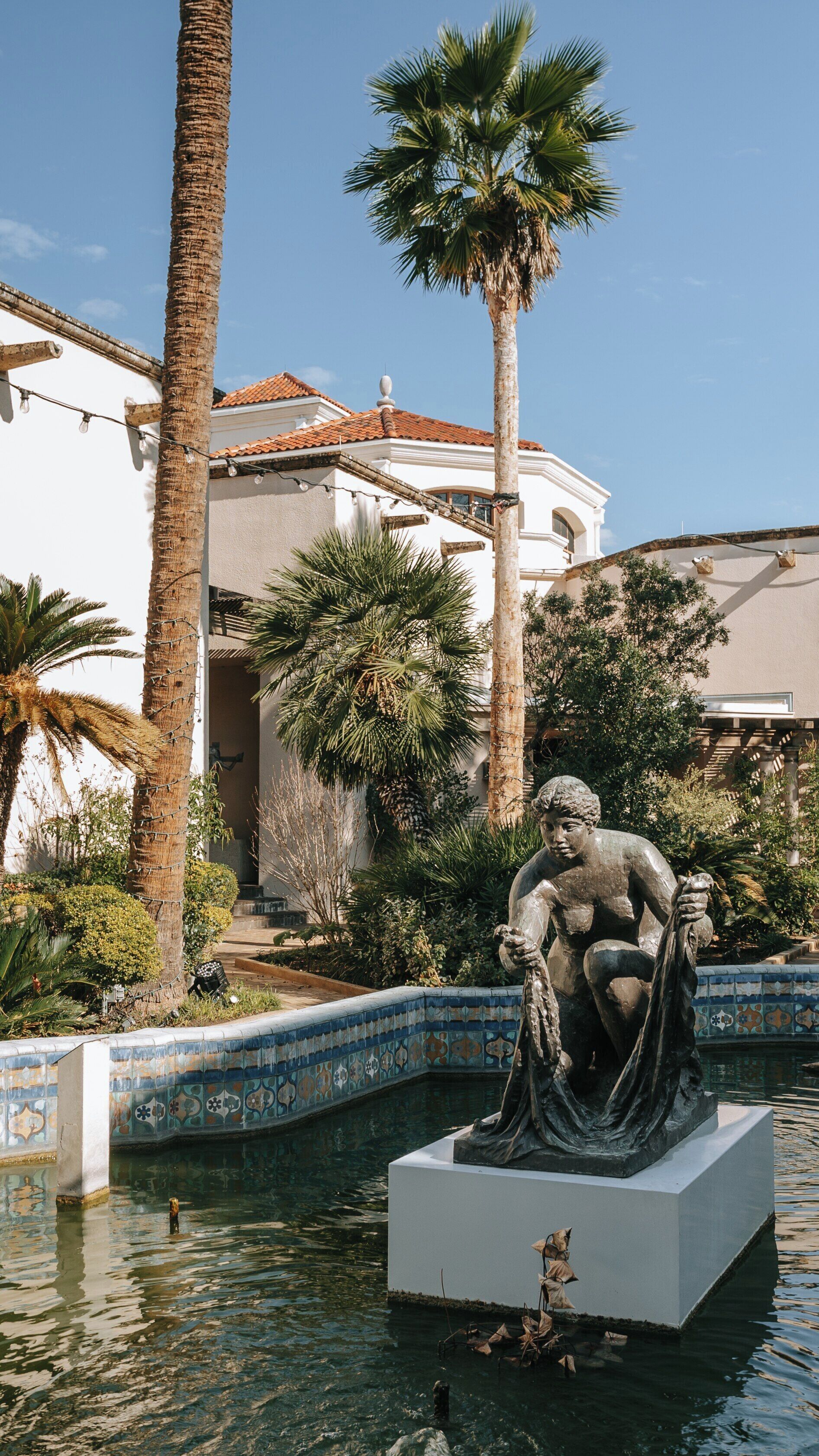 Marion Koogler McNay Art Museum features serene courtyard with sculpture, palm trees, and vibrant landscaping in San Antonio, Texas
