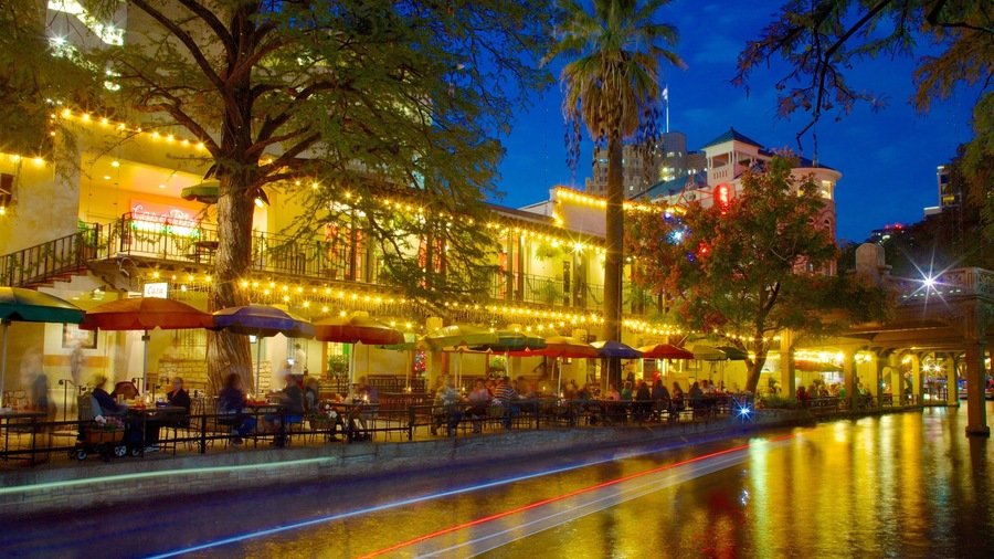 Evening view of San Antonio's vibrant riverside with colorful lights and diners enjoying the atmosphere