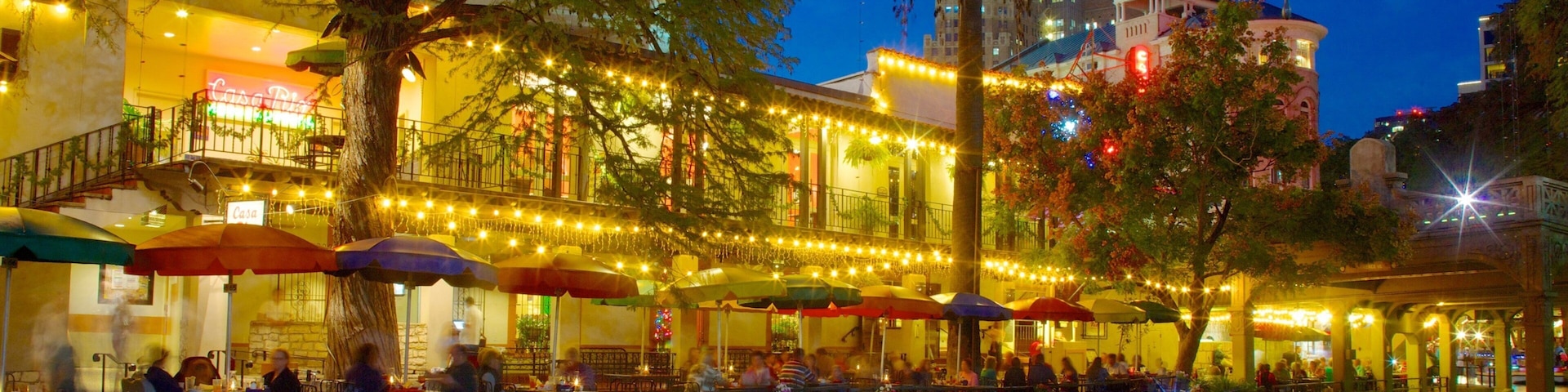 Evening view of San Antonio's vibrant riverside with colorful lights and diners enjoying the atmosphere