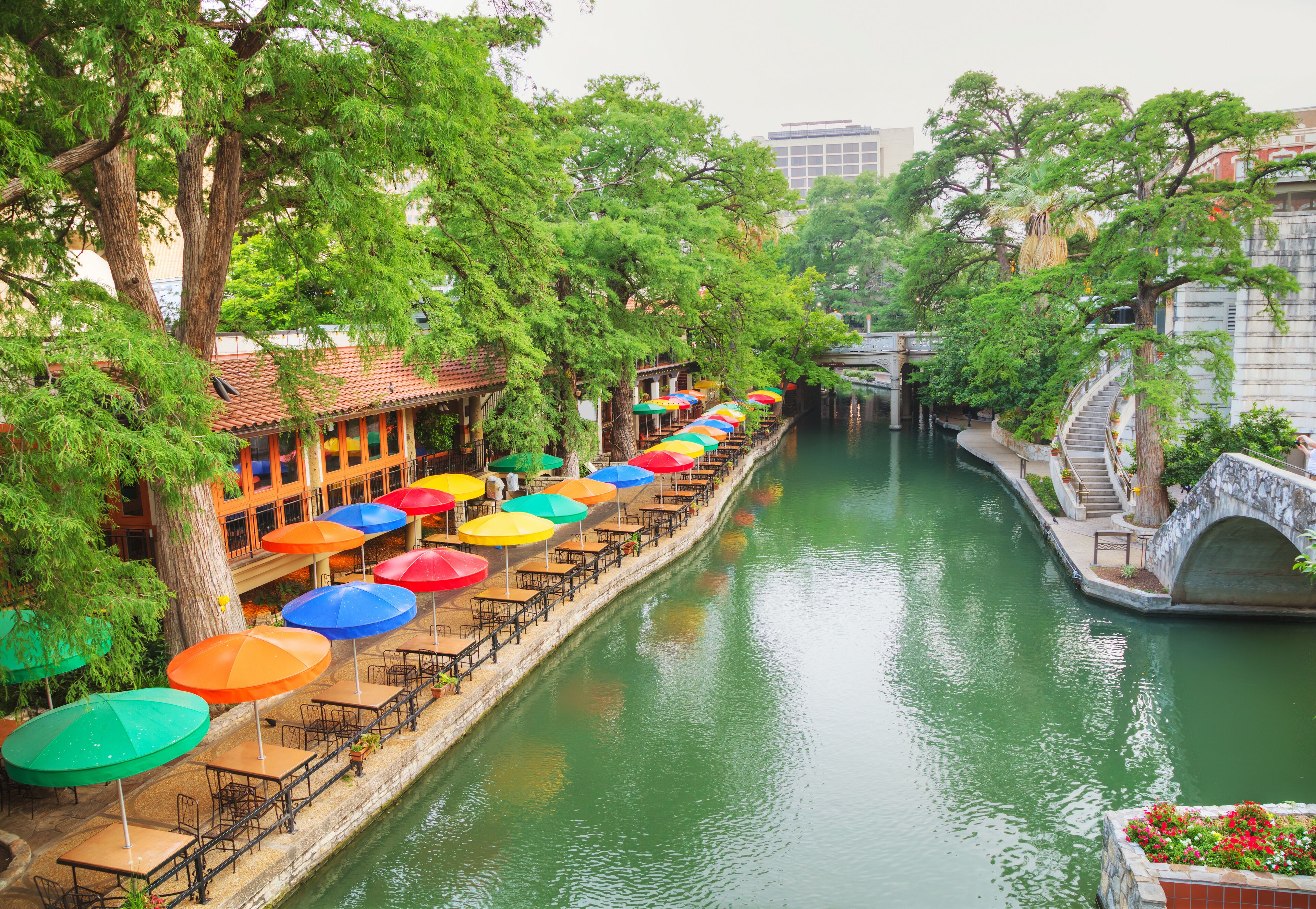 A canal with colorful umbrellas and tables along the banks, surrounded by trees and buildings.