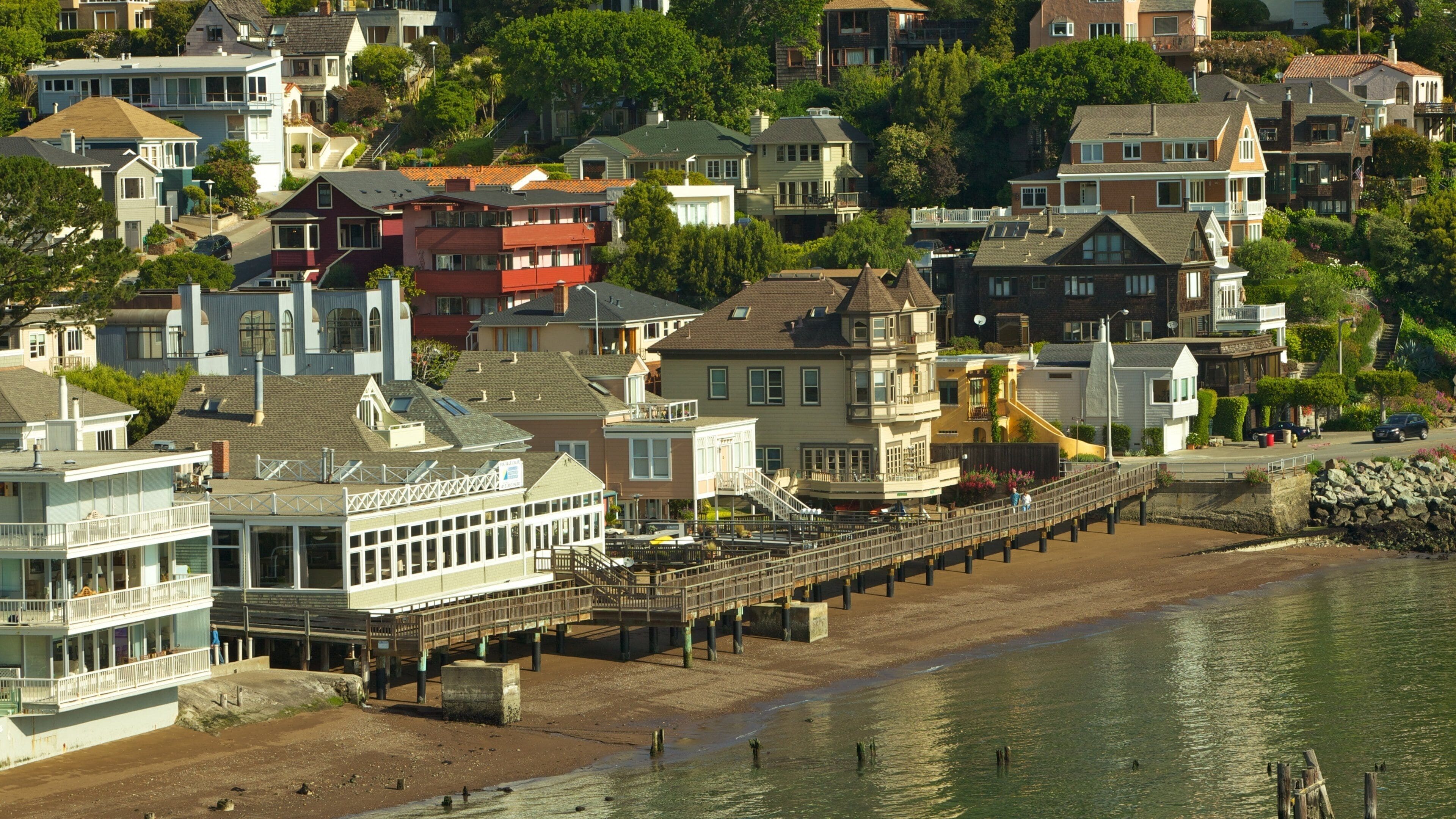 A coastal town with a pier extending into the water, surrounded by colorful houses and lush greenery.