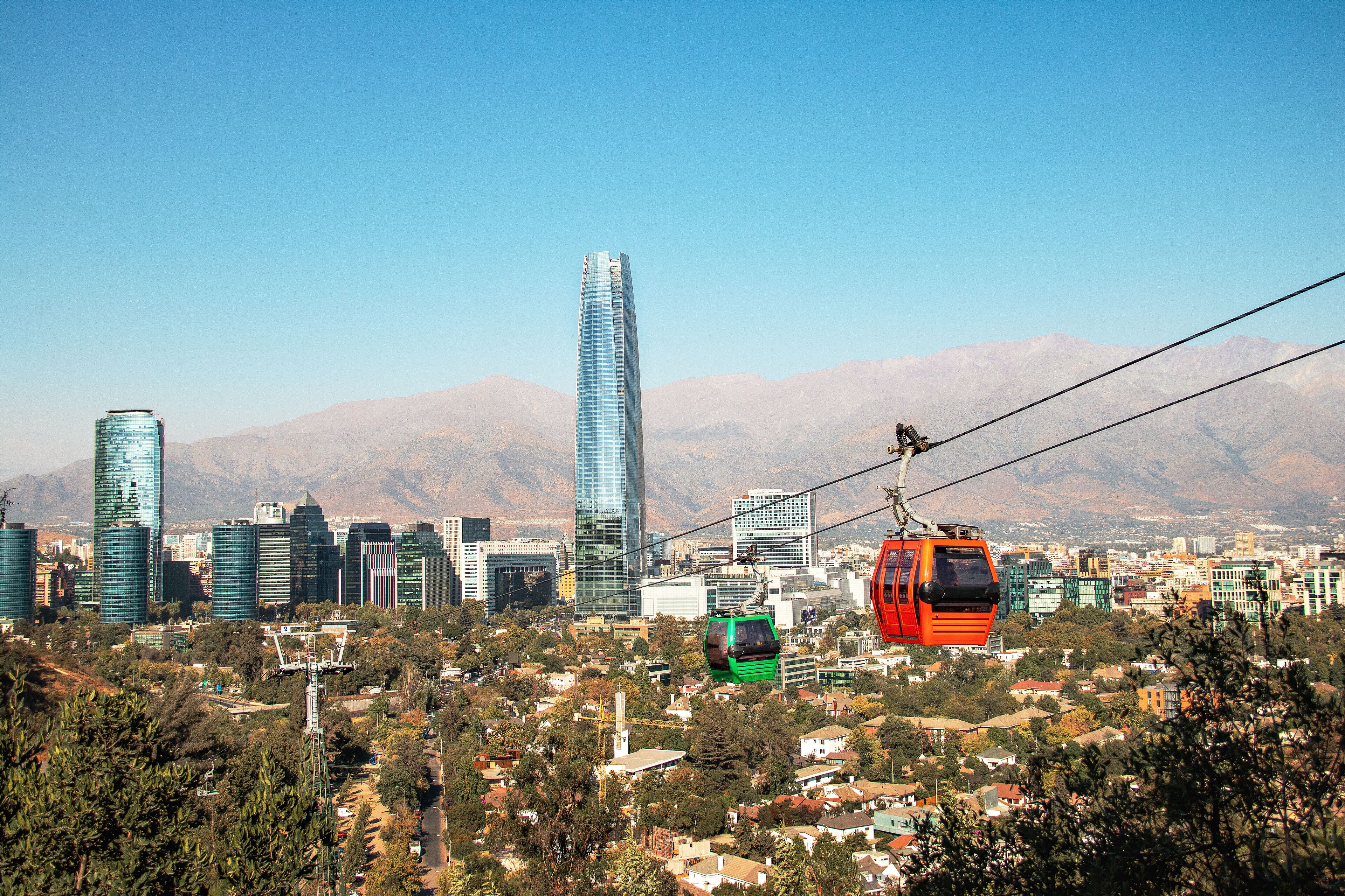 A cityscape with modern skyscrapers, a cable car system, and a mountainous backdrop.