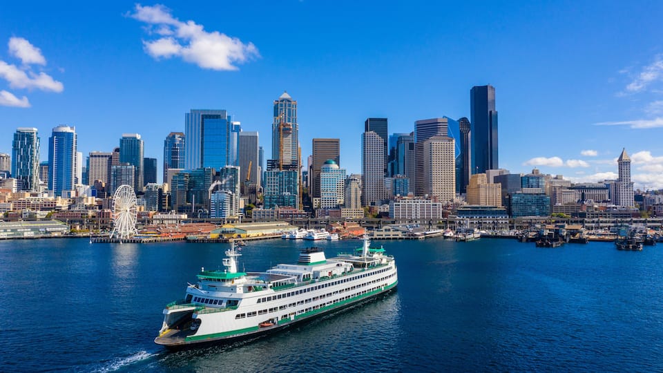 A ferry on a river with a city skyline in the background.