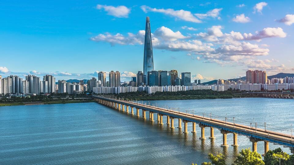 A city skyline with a prominent skyscraper, a long bridge over a river, and surrounding high-rise buildings.
