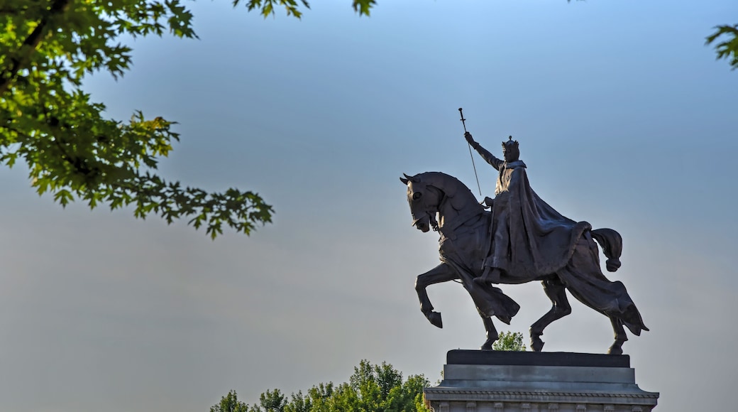 Une statue représentant une figure à cheval, entourée d’arbres et se dressant sous un ciel dégagé.