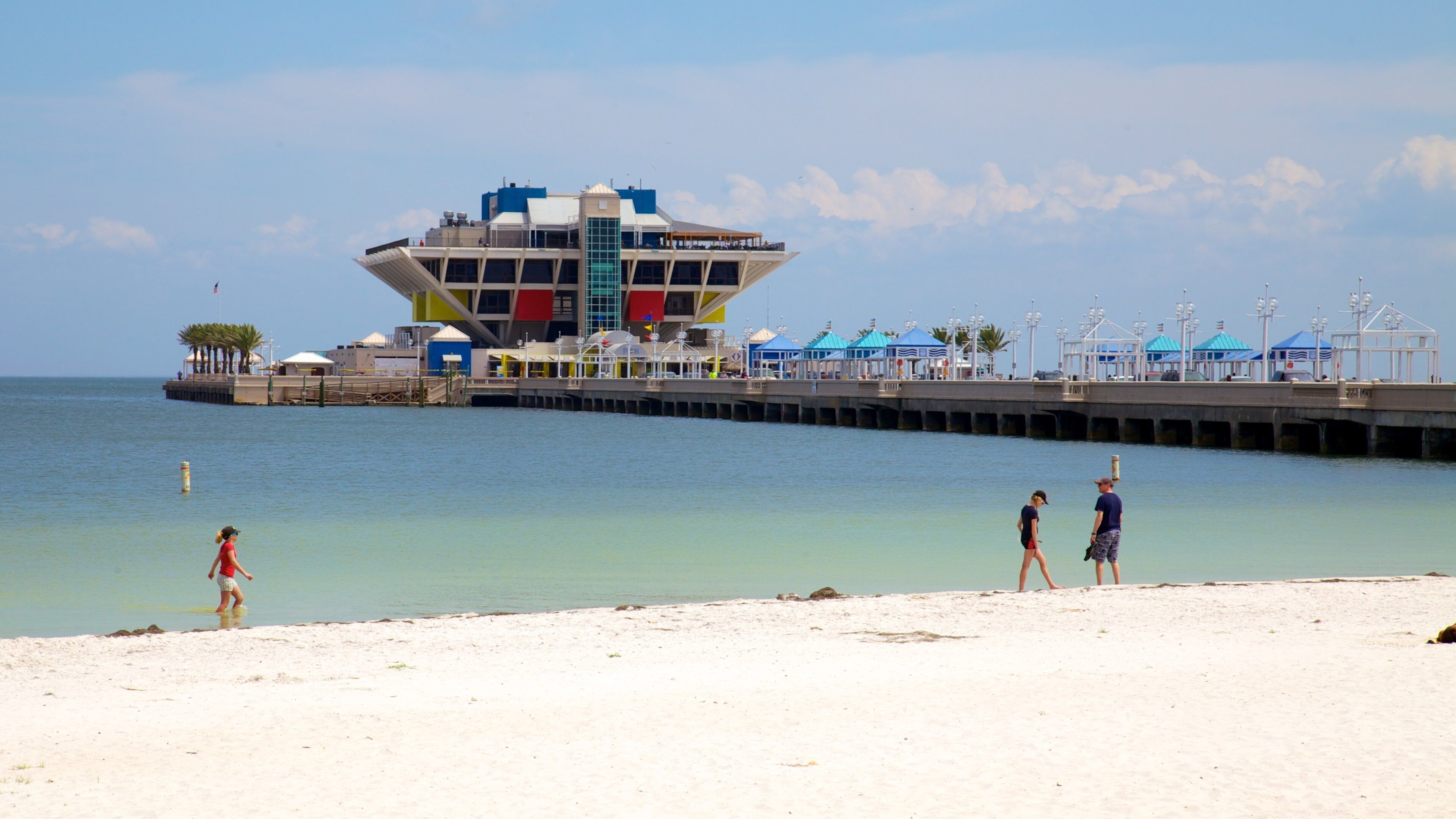 A beach with a pier extending into the water, featuring a colorful building with a unique design.