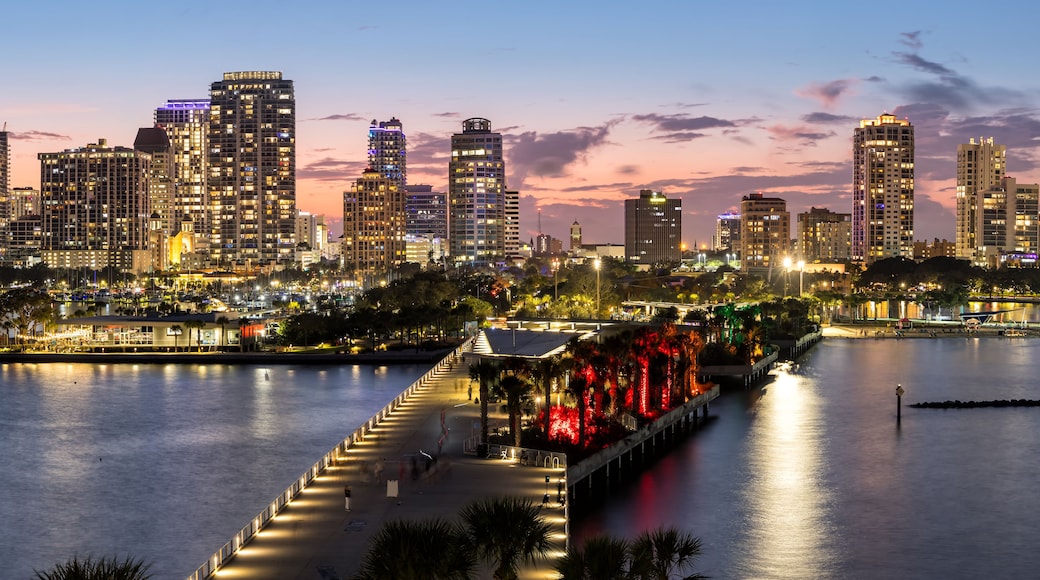 Un horizonte urbano al anochecer, con edificios iluminados y un paseo marítimo.