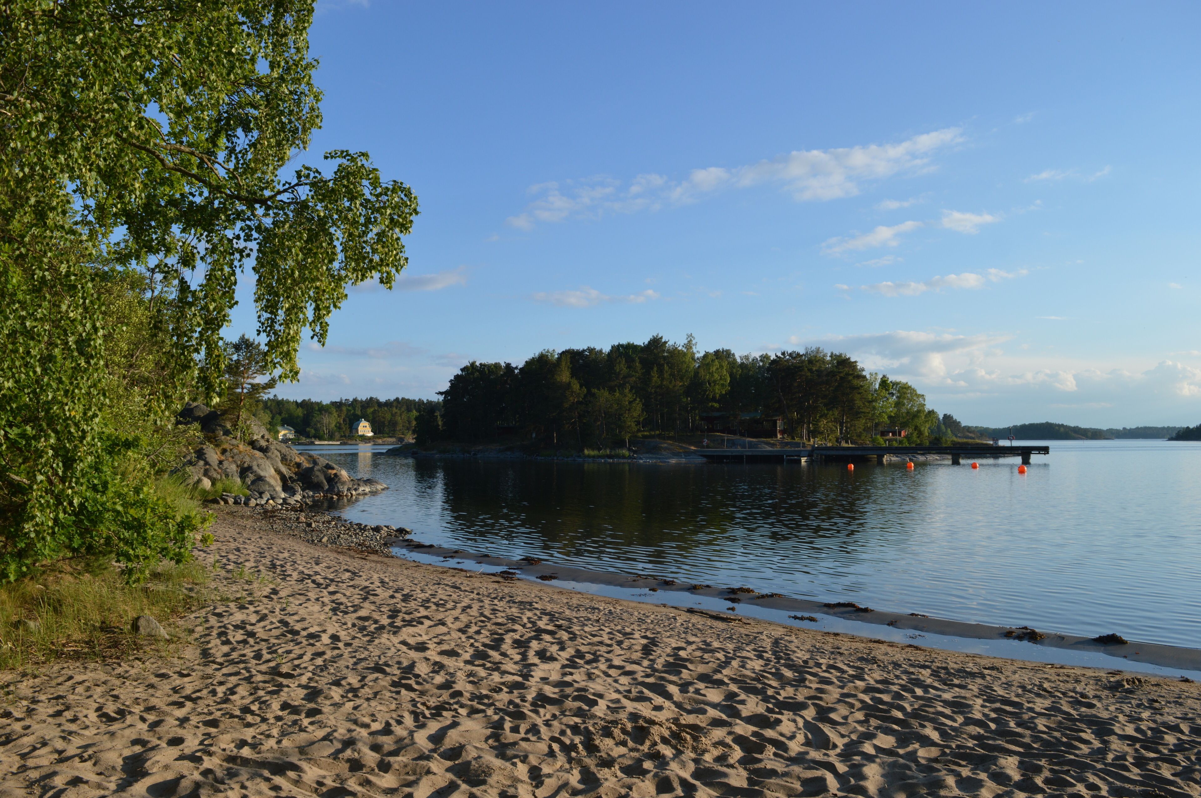 A sandy beach with calm water, a small island with trees, and a clear blue sky.