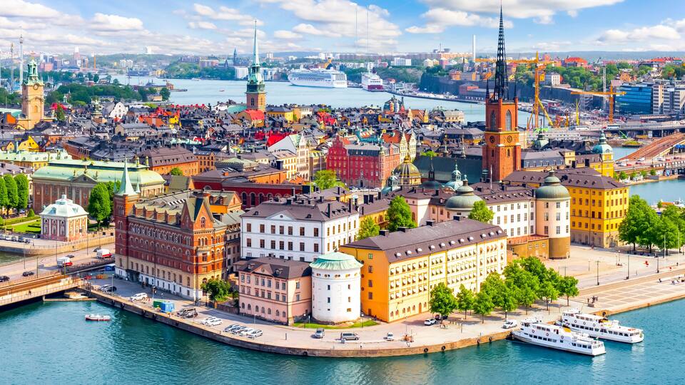 A panoramic view of a city with historic buildings, a prominent church tower, and a large cruise ship docked at the harbor.