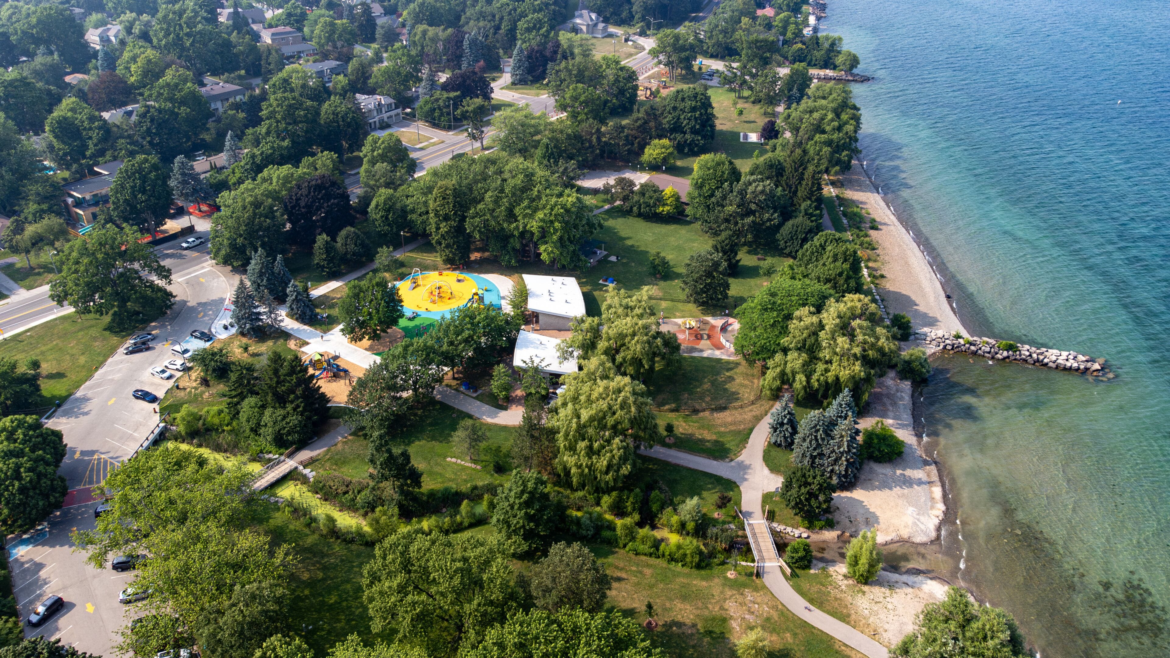 An aerial view of a coastal residential area with a playground, a beach, and a clear view of the water.