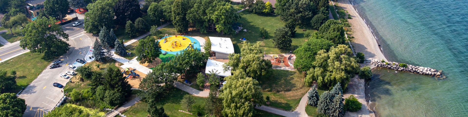 Vista aérea de uma área residencial costeira com um parquinho, uma praia e uma visão clara da água.