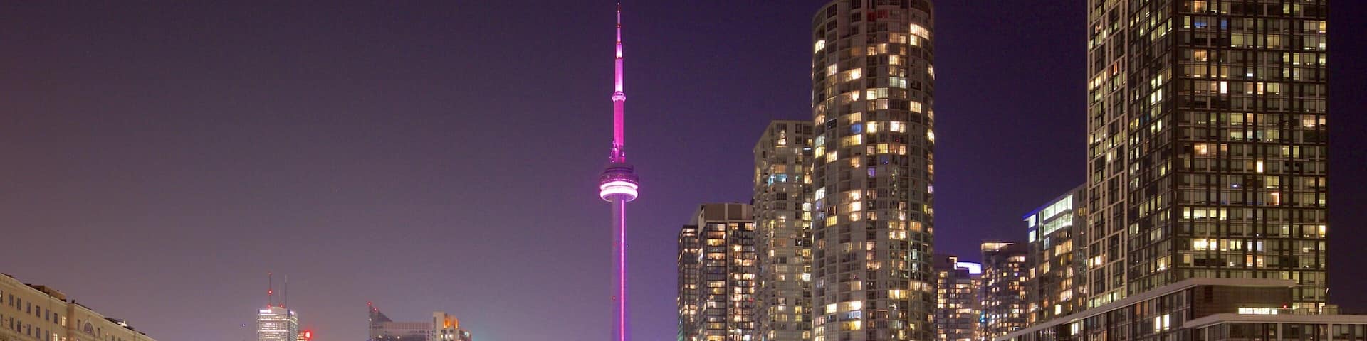 A cityscape at night with a prominent tower lit in purple, surrounded by high-rise buildings and railway tracks.