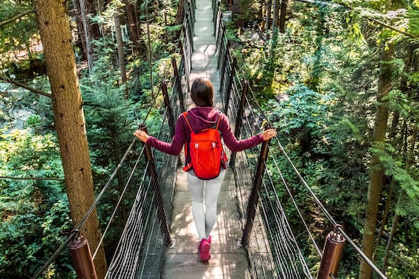 Une personne marchant sur un pont suspendu, entourée d’une forêt dense.