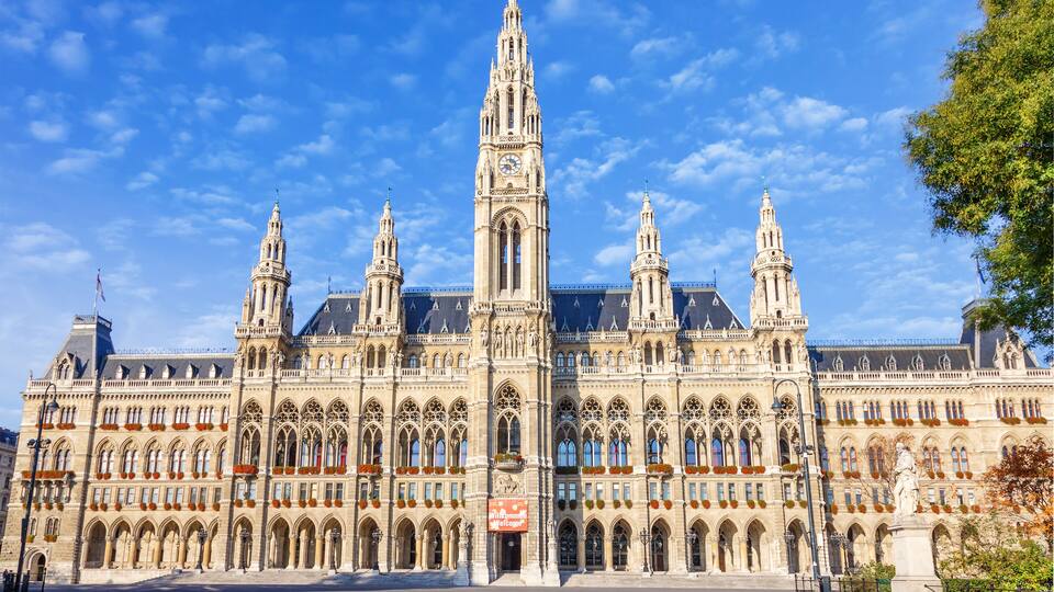A grand historic building with intricate architecture, including a tall central tower and smaller towers, under a clear blue sky.