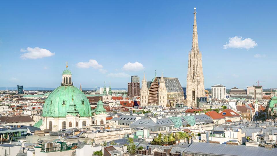 A cityscape with prominent green domed buildings, a tall cathedral, and various modern skyscrapers.