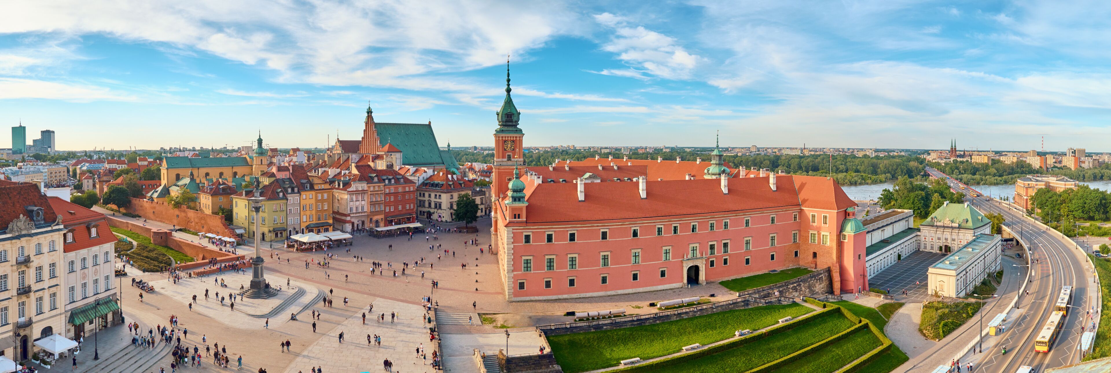 A historic square with a prominent red building, a green-domed tower, and a river in the background.