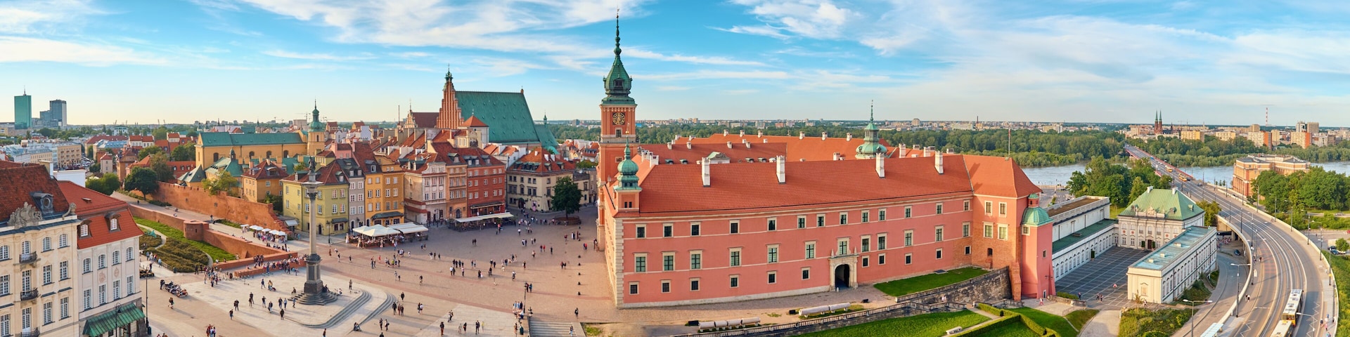 A historic square with a prominent red building, a green-domed tower, and a river in the background.