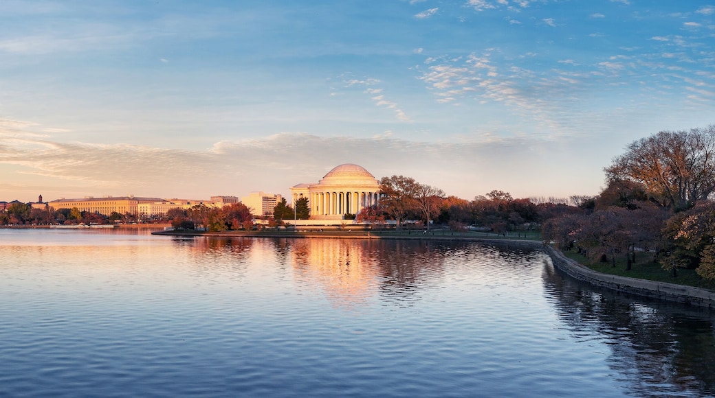 A sunset over a calm lake with a Washington Monument and a domed building reflecting on the water.