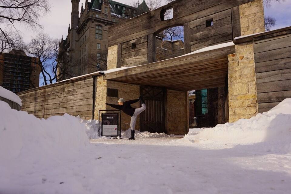 Una persona realizando una postura de yoga frente a un edificio de madera con nieve en el suelo.