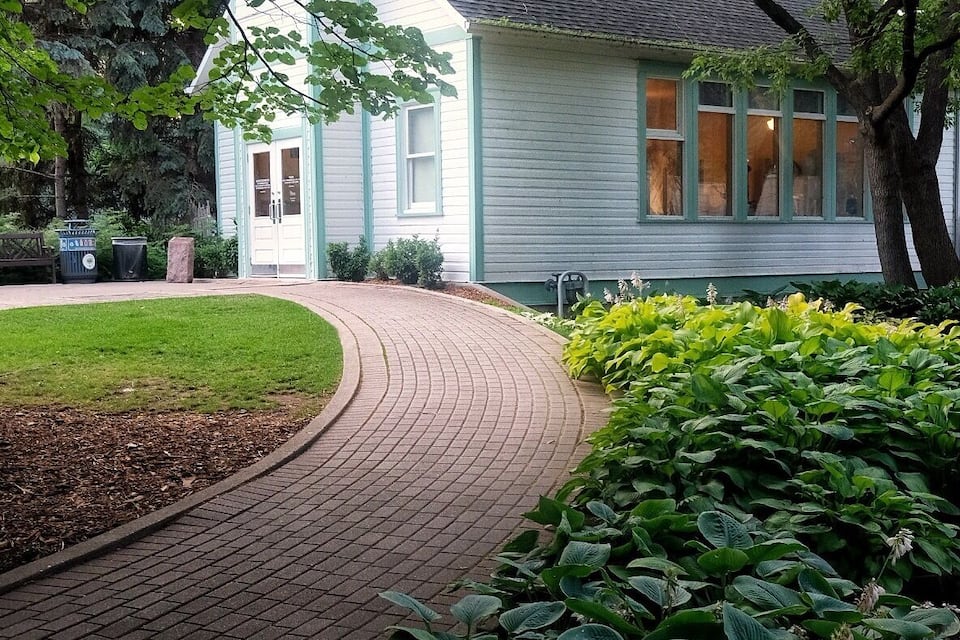 Una casa amb un camí de maons que hi convergeix, envoltada de vegetació abundant i un jardí ben cuidat.