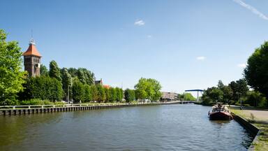 A river with a boat, a bridge, a tower, and trees along the banks.