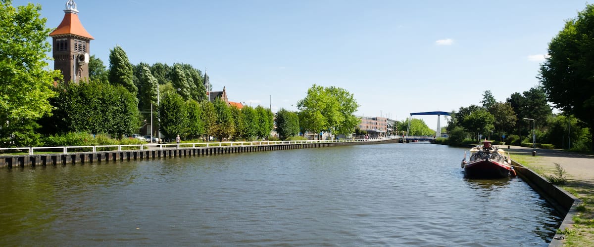 A river with a boat, a bridge, a tower, and trees along the banks.