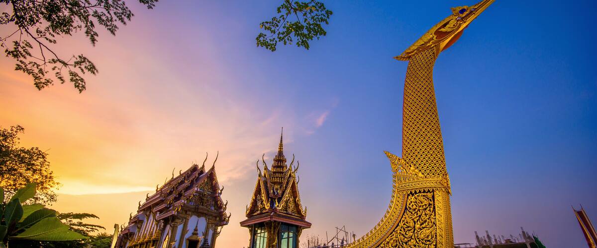 A golden boat-shaped structure with intricate designs, a smaller temple, and a bridge in the background.