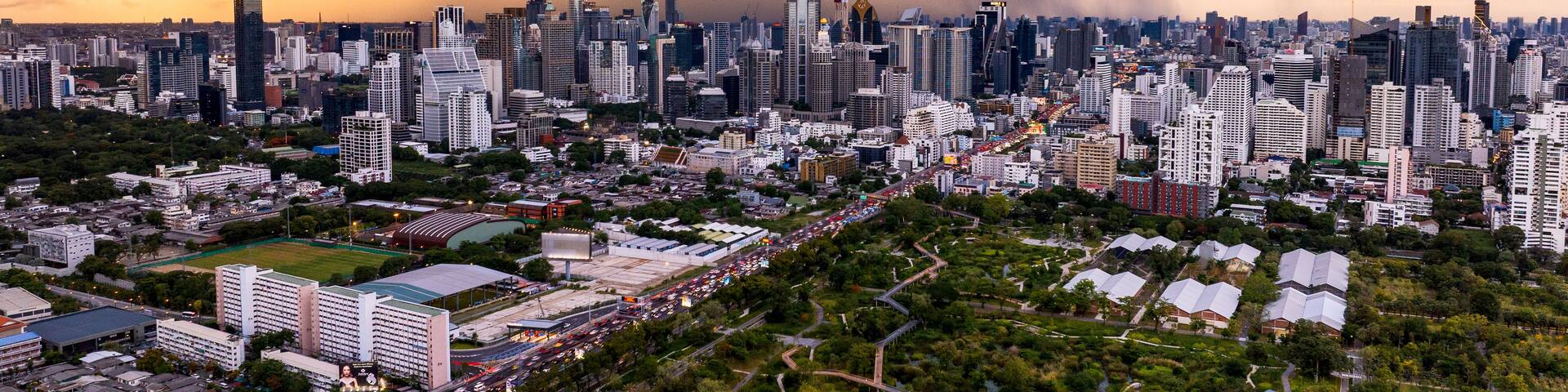 Bangkok, Thailand - 20 June 2024: Aerial view of the Bangkok skyline and Benjakitti Park in Khlong Toei under a dramatic dark storm cloud at sunset, featuring tall skyscrapers and lush green parkland.