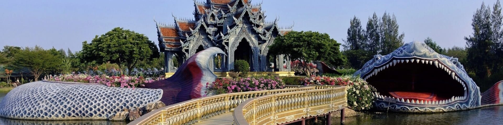 A bridge with golden railings, a temple with a dragon-shaped roof, and a large dragon sculpture in the water.