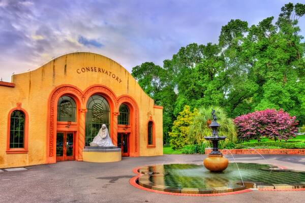 A conservatory with a statue, a fountain, and lush greenery.