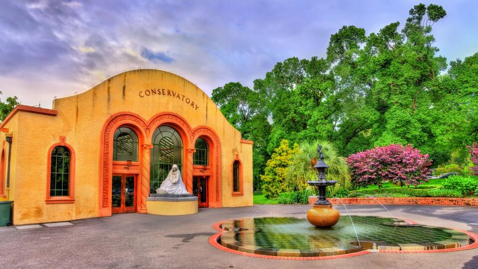 A conservatory with a statue, a fountain, and lush greenery.