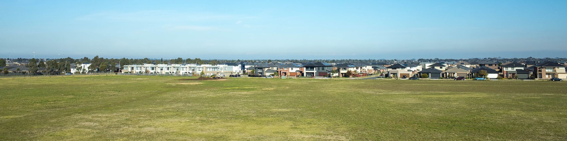 Background texture of large vacant land and residential houses in the distance. Concept of real estate development, the housing market, and new suburb. Point Cook, Melbourne, VIC Australia.