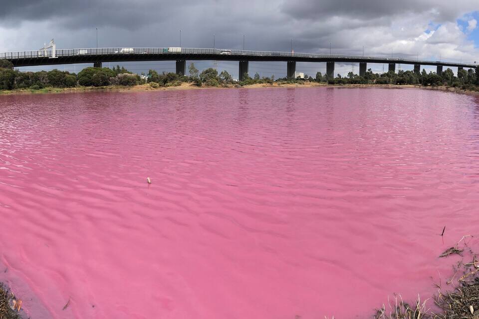 Un río de agua rosada, un puente y un cielo nublado.