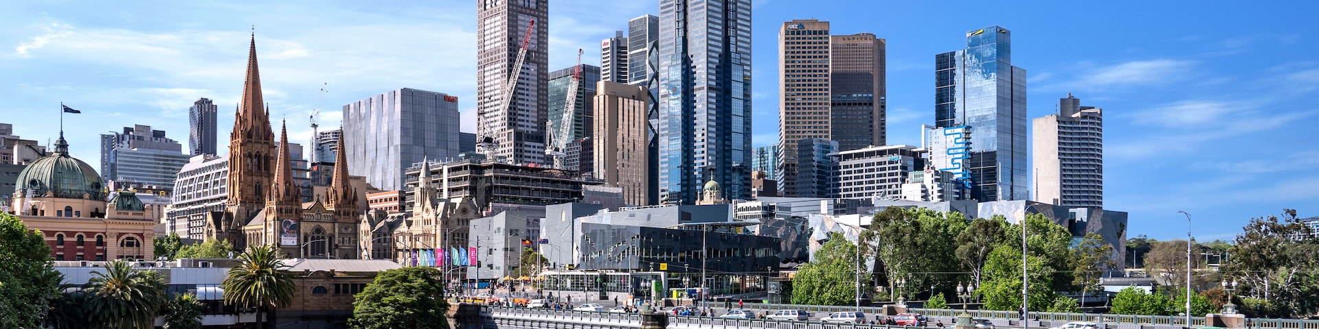 Une vue sur les toits d’une ville, avec des gratte-ciel modernes, une cathédrale historique et une rivière traversée par un pont.