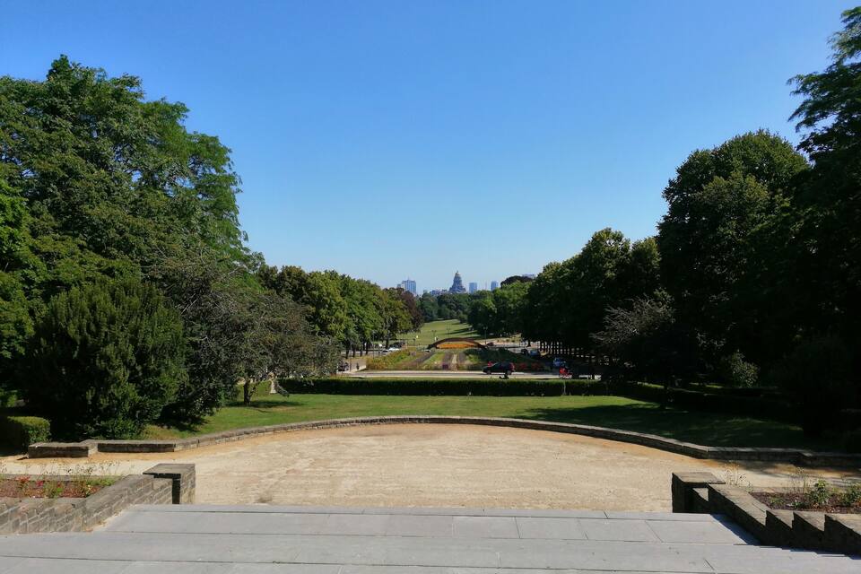 A park with a large open space, trees, and distant city buildings.