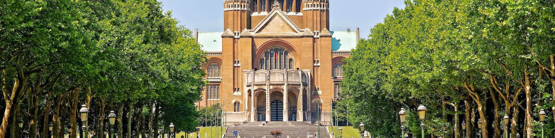 A large historic building with a prominent dome and twin towers, surrounded by a well-maintained park with trees and manicured lawns.