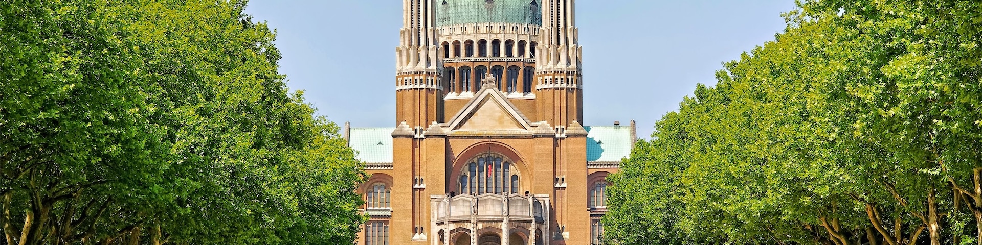 Um edifício histórico imponente com uma cúpula grande e duas torres geminadas, cercado por um parque bem cuidado com árvores e gramados aparados.