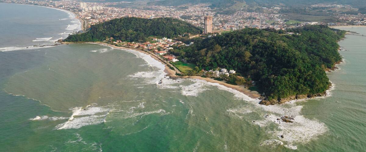 An aerial view of a coastal city with a prominent hill, dense forest, and a beach.