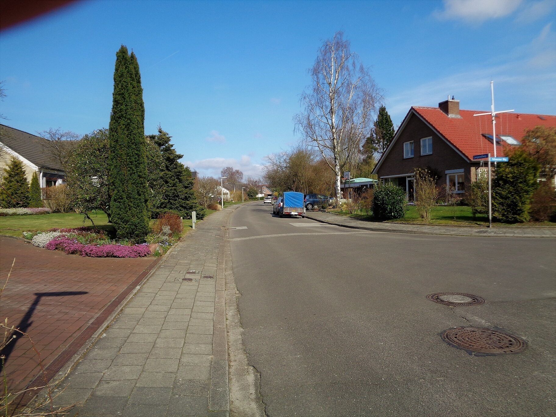 A residential street with houses, a sidewalk, and a blue truck parked on the side.