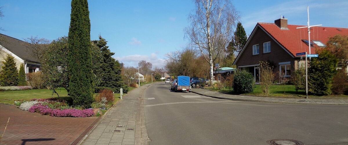 A residential street with houses, a sidewalk, and a blue truck parked on the side.